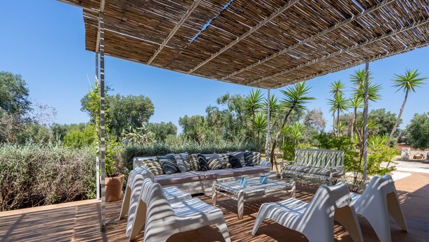 Un espacio al aire libre con techo de paja, un sofá y sillas blancas.
