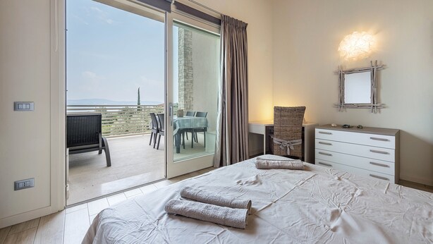 Een slaapkamer met een bed, een kaptafel, een nachtkastje, een spiegel en uitzicht op de omgeving.