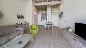 Een woonkamer met een bank, een groene fauteuil, een salontafel, een televisie en een keuken op de achtergrond.