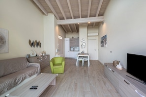 Un salon avec un canapé, un fauteuil vert, une table basse, un téléviseur et, au fond, une cuisine.