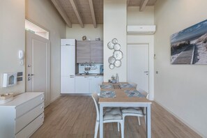 Et kompakt køkken med et køleskab, et spisebord med stole, en vægmonteret aircondition og en dekorativ vægdekoration.