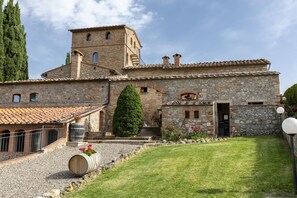 A stone building with a tiled roof, a central tower, and a well-maintained lawn.