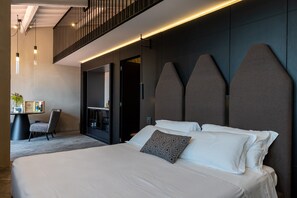 Une chambre d’hôtel moderne avec un grand lit, un bureau avec une chaise, une petite table avec une plante et un balcon doté d’une rambarde.