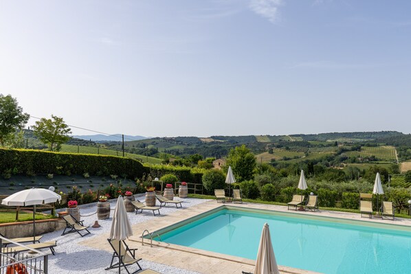 A pool with lounge chairs and umbrellas, surrounded by greenery and a scenic view.