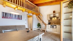 Una cocina moderna con vigas de madera, un comedor con mesa y sillas, y una escalera que sube a un nivel superior.