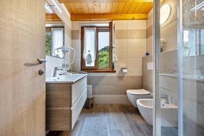 Ein modernes Badezimmer mit Holzboden, einem Fenster mit Vorhängen, einem Waschbecken, einer Toilette und einem Bidet.