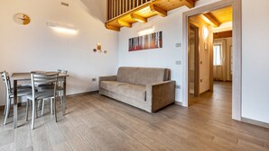 Una sala de estar moderna con piso de madera, un sofá, una mesa de comedor con sillas y una escalera.