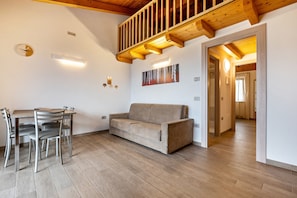 Una sala de estar moderna con piso de madera, un sofá, una mesa de comedor con sillas y una escalera.