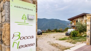 Señal de 'Agriturismo Bocca Neves' con vistas a montañas y un edificio con balcón.