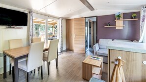 A modern living room with a dining area, a sofa, a TV, and a kitchen counter. - Mobile Home for 6 Guests with Shared Pool and Private Terrace (Saint-Brevin-les-Pins)