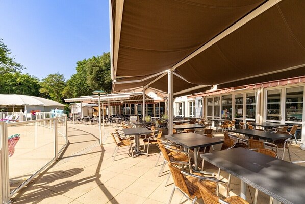 An outdoor café with tables and chairs, covered by large umbrellas, and a glass building in the background.