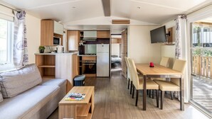 A compact living space with a kitchenette, a dining area, and a seating area with a sofa and coffee table. - Mobile Home for 6 Guests with Shared Pool and Private Terrace (Saint-Brevin-les-Pins)