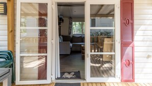 A house with a sliding glass door entrance, a red shutter, and a visible living room with a couch and a coffee table. - Mobile Home for 6 Guests with Shared Pool and Private Terrace (Saint-Brevin-les-Pins)