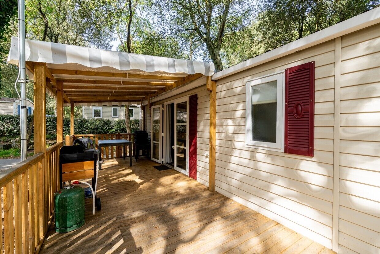 A covered outdoor deck with a grill, a table, and chairs, and a sliding glass door leading to a covered patio area.