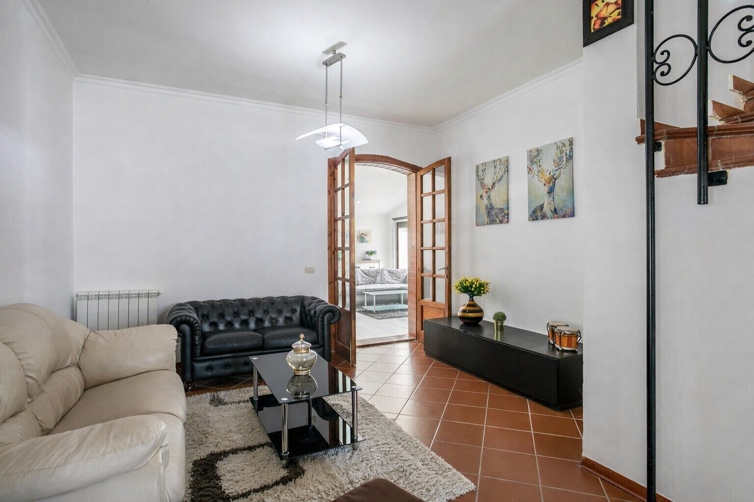 Ein Wohnzimmer mit schwarzem Sofa, einem beigen Sessel, einem kleinen Tisch mit einer Vase und einer schwarzen Konsolentisch mit Dekoration.