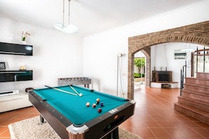 Une table de billard dans une pièce avec une arche en briques, un canapé et un téléviseur.