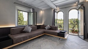Een moderne woonkamer met een hoekbank, een bijzettafeltje en uitzicht op het buitengebied door grote ramen.