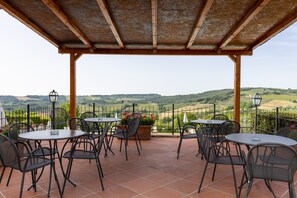 Une terrasse avec des tables et des chaises, une pergola et une vue sur des collines ondoyantes.