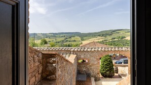 Un patio de piedra con una mesa y sillas, un árbol en maceta y vistas a colinas ondulantes.