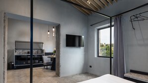 Una habitación de hotel moderna con una cama grande, un televisor montado en la pared, una ventana con cortinas y una zona de estar con una mesa y sillas.