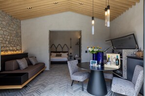 Habitación de hotel moderna con sofá, mesa de comedor, sillas, cama y una pared de piedra.