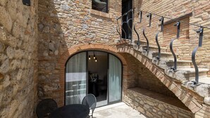 Un bâtiment en pierre doté d’un escalier, d’une entrée avec une porte vitrée et d’une table entourée de chaises.