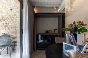 A hotel room with a stone wall, a dining area with metal chairs, a black table, a kitchen area, and a vase with flowers.