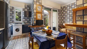 A compact kitchen with a washing machine, a dining area with a table and chairs, and a TV on a stand. - Apartment 'Il Giardino Di Giò' with Mountain View, Private Terrace and Wi-Fi (Finale Ligure)