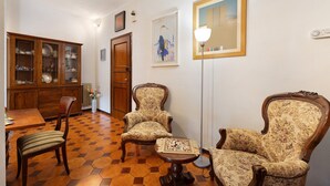 A dining area with a wooden cabinet, two upholstered chairs, a table, and a floor lamp. - Apartment 'Il Giardino Di Giò' with Mountain View, Private Terrace and Wi-Fi (Finale Ligure)