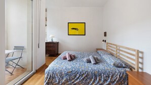 A bedroom with a bed, a wooden headboard, a small bedside table, a nightstand, a chair, a desk, and a sliding glass door leading to a balcony. - Apartment 'Il Giardino Di Giò' with Mountain View, Private Terrace and Wi-Fi (Finale Ligure)