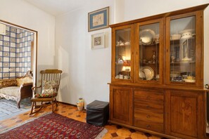 Una habitación con una mecedora, un aparador con puertas de cristal, un tapete estampado y suelo de baldosas.