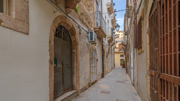 A narrow street with buildings on either side, featuring arched doorways and barred windows. - Holiday Apartment 'Cheyenne's House' with Terrace, Balcony & Wi-Fi (Siracusa)