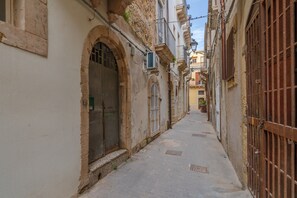 Una calle estrecha flanqueada por edificios, con puertas abovedadas y ventanas con rejas.