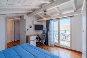 Un dormitorio con cama, escritorio con silla, televisor y puerta corrediza de vidrio a un balcón.