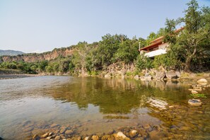 A river with clear water, rocks, and a building with a red roof on a hillside.