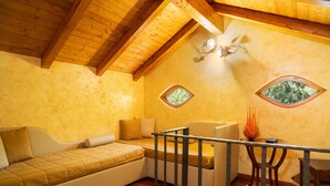 Ein gemütliches Schlafzimmer im Dachgeschoss mit Holzbalkendecke, einer Schlafcouch, einem kleinen Tisch und zwei Fenstern mit Blick ins Grüne.