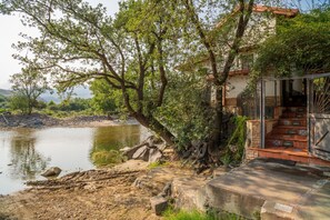 A riverside property with a stone staircase leading to a wooden door, surrounded by trees and a calm river. - Holiday Home 'Teleferica' with Mountain View, Wi-Fi and Air Conditioning (Bronte)