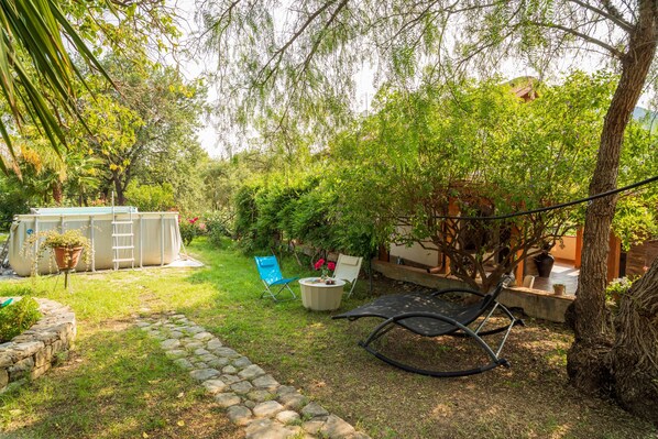 A garden with a hammock, a blue chair, and a white chair. There is a small table with a potted plant.