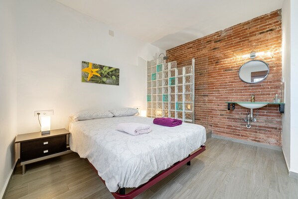 Un dormitorio con una cama, una mesita de noche, un espejo en la pared, una lámpara colgante y una pared de ladrillo.