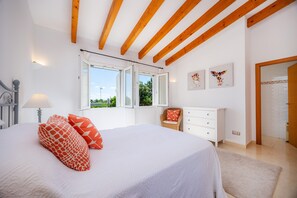 Un dormitorio con cama, una silla, un aparador y una ventana con persiana abierta.