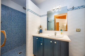 Un baño con ducha de azulejos azules, un lavabo con espejo y armarios azul oscuro.