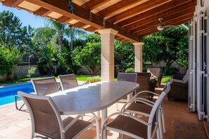 Un patio exterior con piscina, asientos cubiertos y una pérgola.