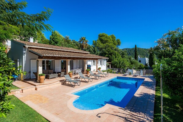 Una casa con piscina, mobiliario de exterior y jardín.