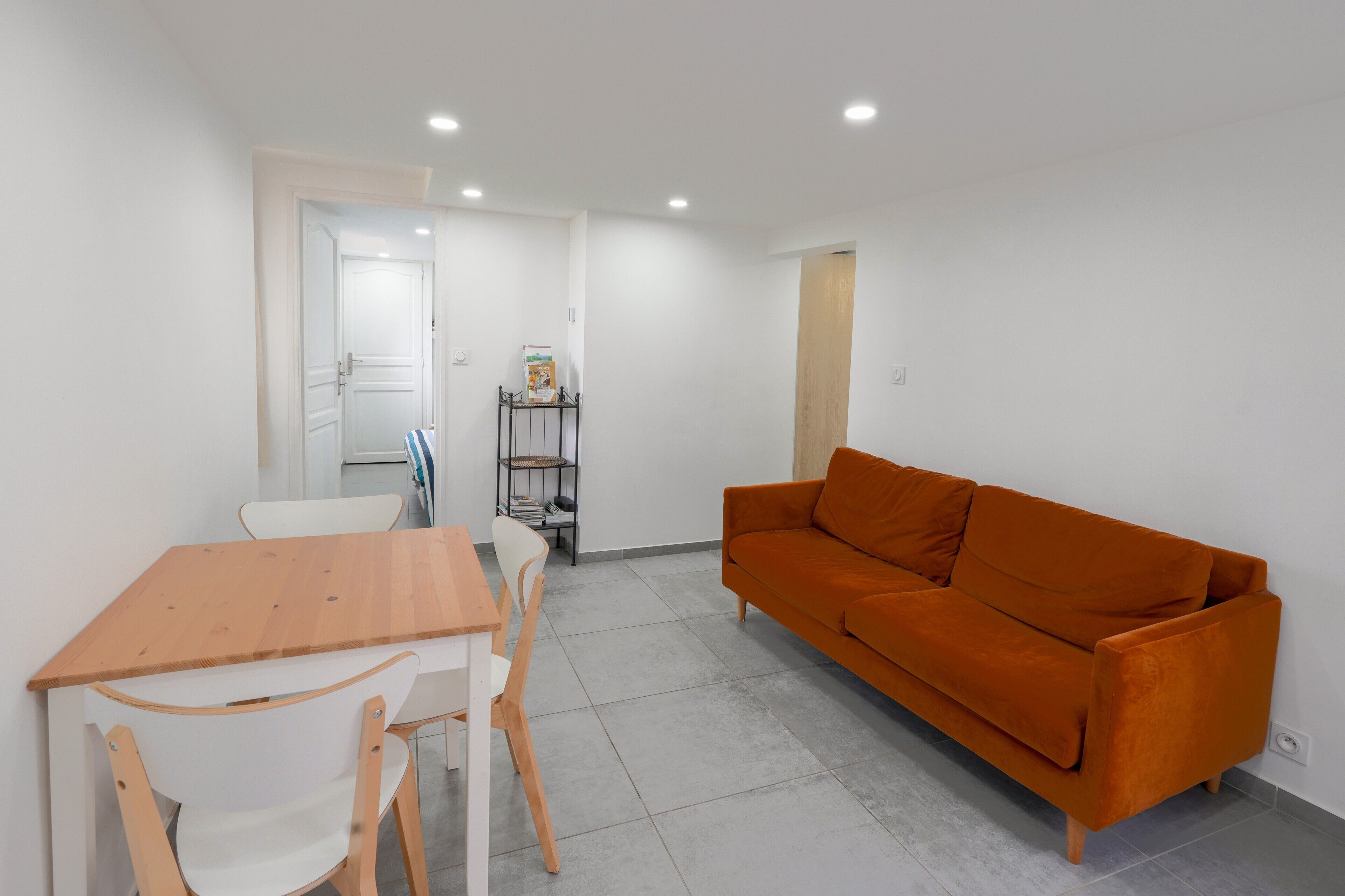 A room with a wooden table, white chairs, an orange sofa, and a bookshelf.