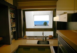 Une cuisine avec une fenêtre donnant sur la mer, un évier et une étagère remplie de bocaux.
