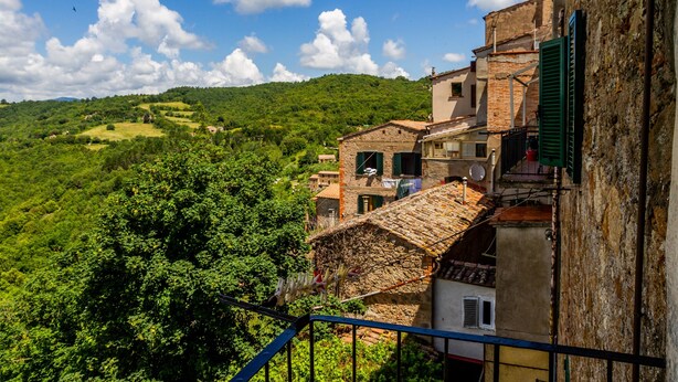 Un village perché sur une colline, avec ses bâtiments traditionnels en pierre, un balcon offrant une vue imprenable et un ciel d’un bleu éclatant.