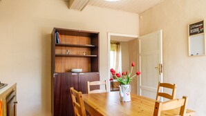 Un coin repas avec une table en bois, des chaises, une bibliothèque et un vase rempli de fleurs rouges.