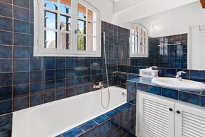 Une salle de bain avec une baignoire, un lavabo et une fenêtre donnant sur l’extérieur.