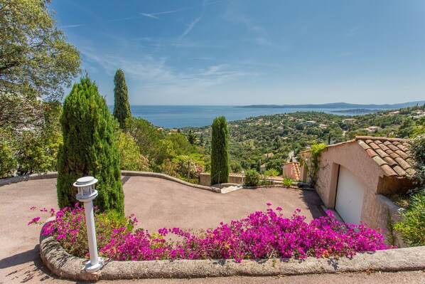 Un jardin aménagé avec un lampadaire, des fleurs aux couleurs vives et une vue sur la mer et les collines lointaines.