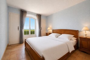 A bedroom with a large bed, two bedside tables with lamps, a window with curtains, and a door. - Villa Bellevue with Panoramic Views · South-Facing · Overlooking Saint-Tropez (Roquebrune-sur-Argens)